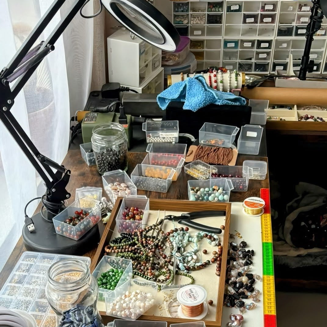 Pearl Art Nature jewellery-making workbench with sorted gemstone beads, baroque pearls, jewellery pliers and tools, organised in clear boxes under a magnifying lamp