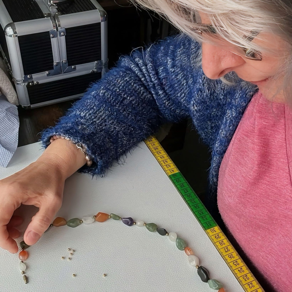 Ewa from Pearl Art Nature arranging a handmade gemstone necklace on a workbench, measuring the length with a tape measure