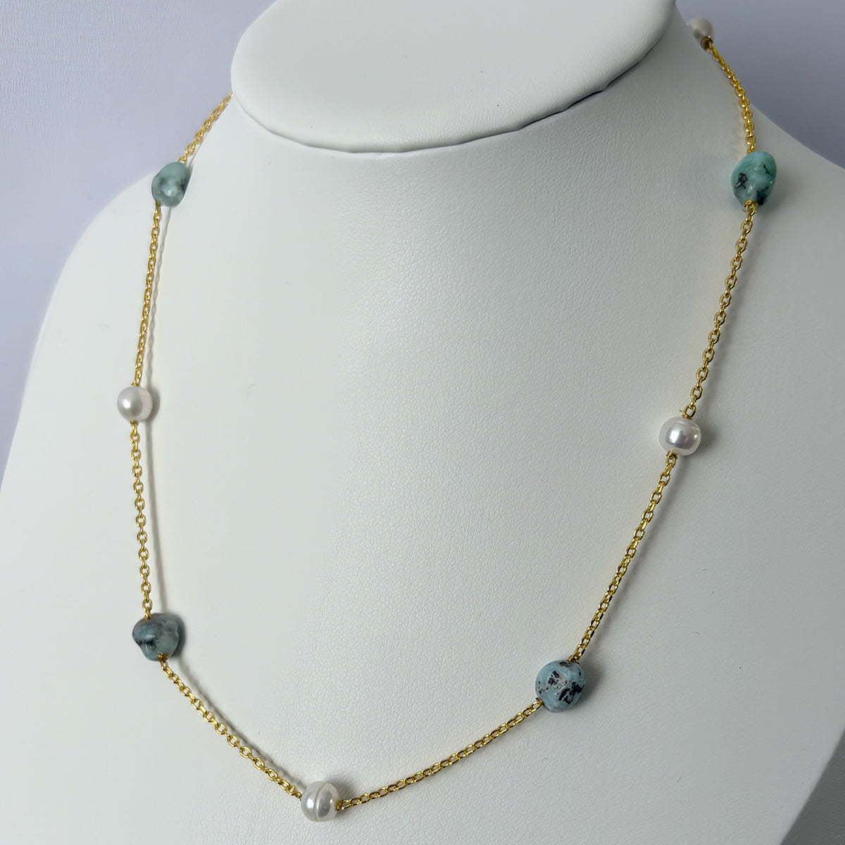 White baroque pearls and blue-grey larimar stones alternating along a gold-filled chain, displayed on an angled white jewellery bust.