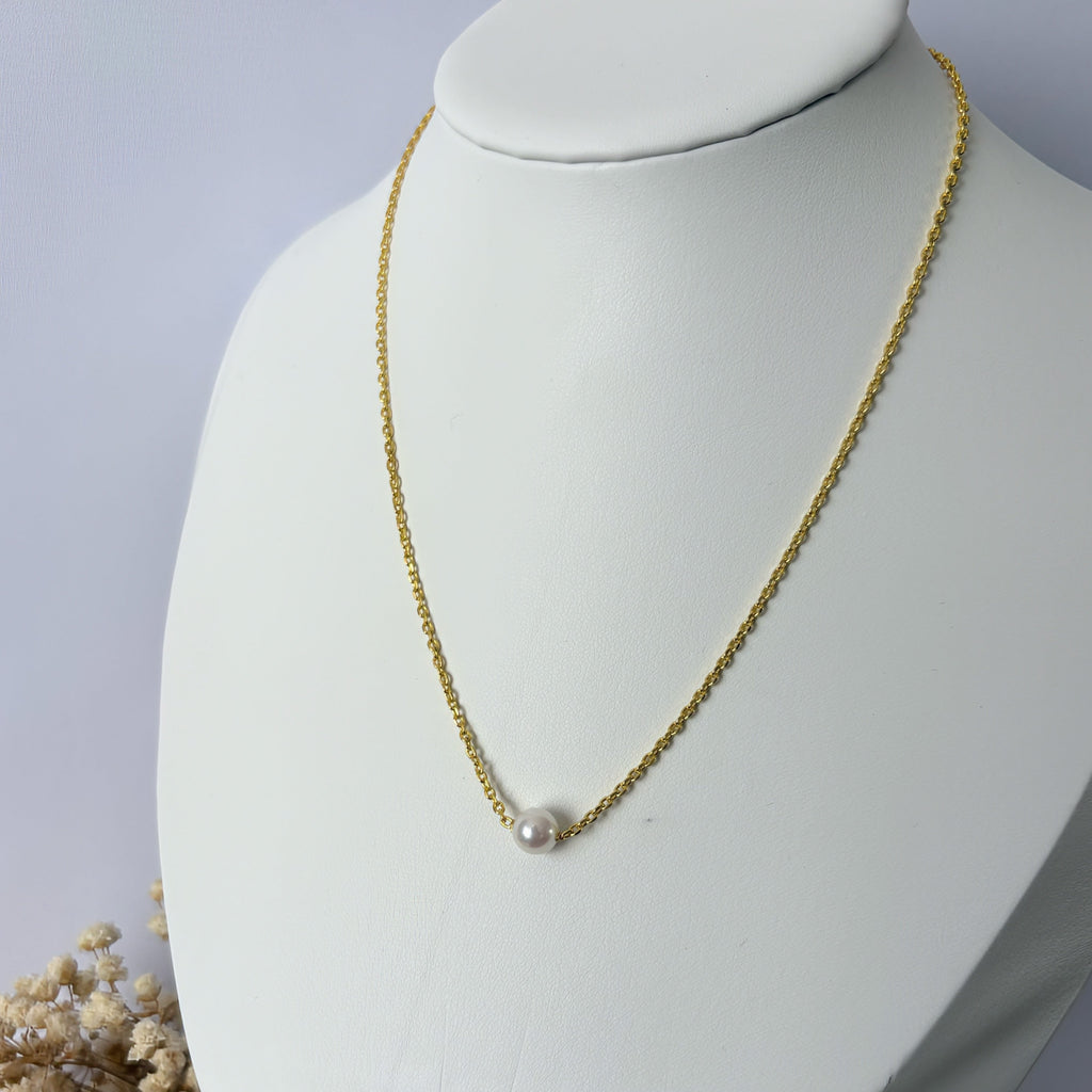 Single white Akoya pearl on a gold-filled chain, displayed on an angled white jewellery bust with dried flowers at its base.