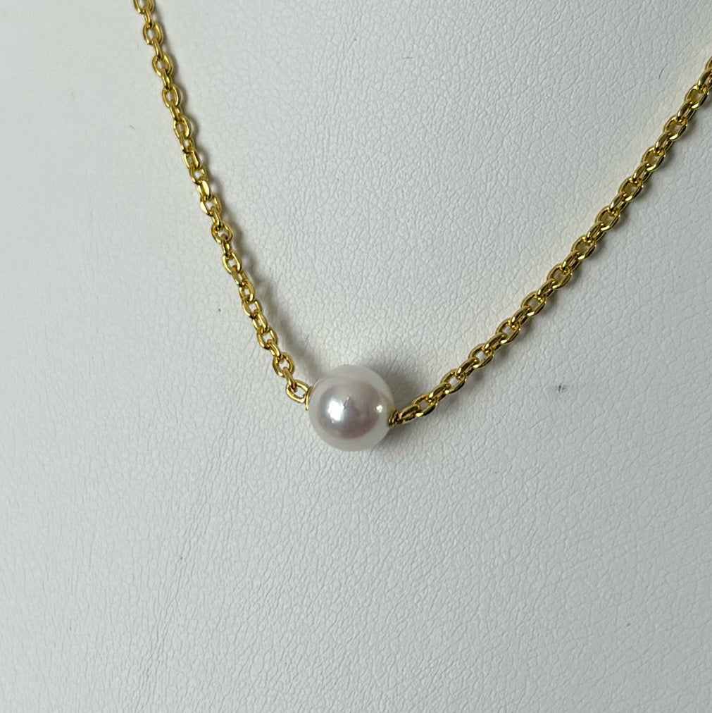 Close-up of a single lustrous white Akoya pearl set directly on a gold-filled chain against a white jewellery bust.