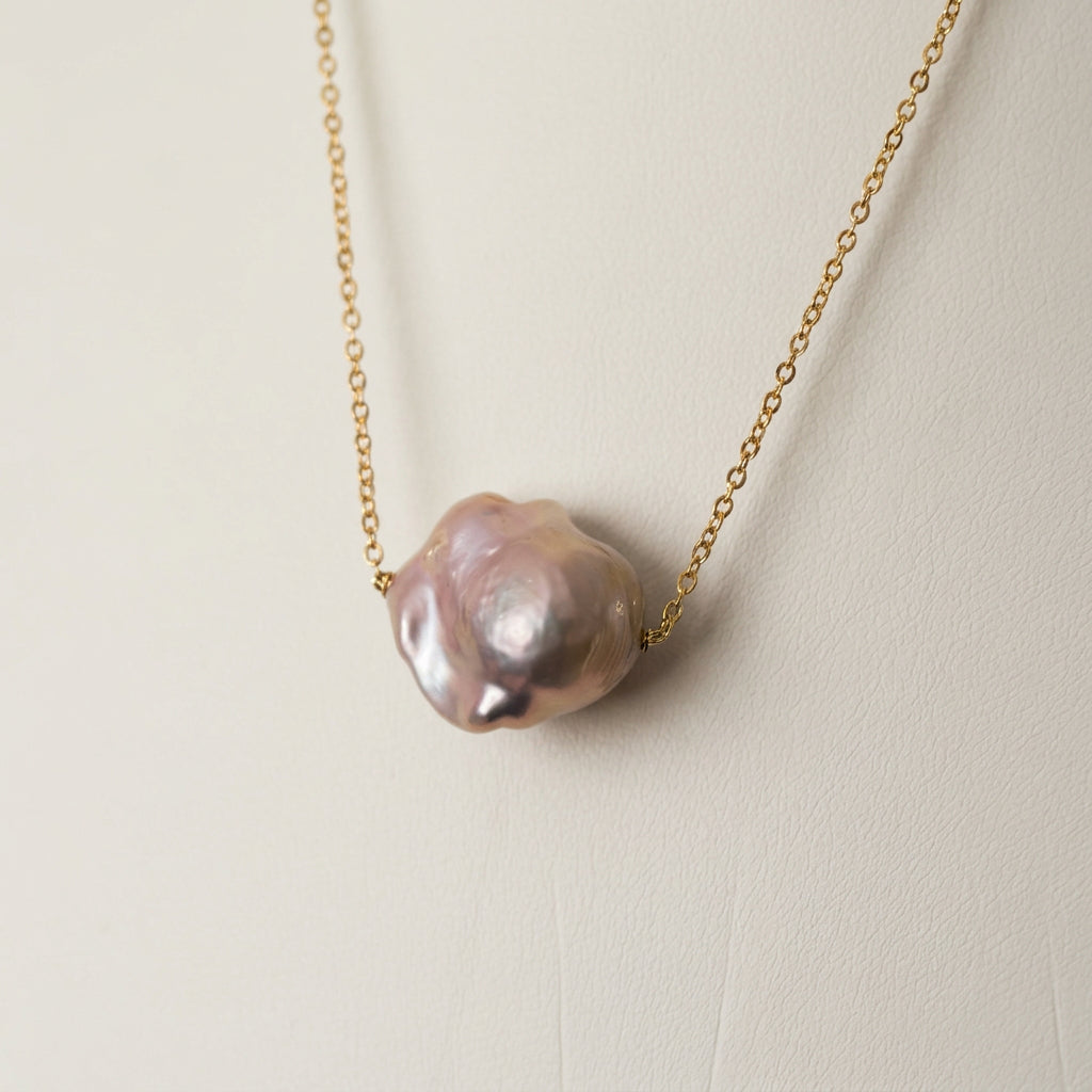 Close-up of a pink Keshi pearl on a fine gold-filled chain against a white jewellery bust, showing its irregular rounded shape and blush-mauve lustre.