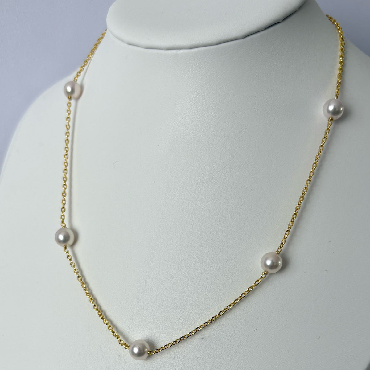 Close-up of five lustrous white Akoya pearls evenly spaced along a gold-filled chain, displayed on a white jewellery bust.