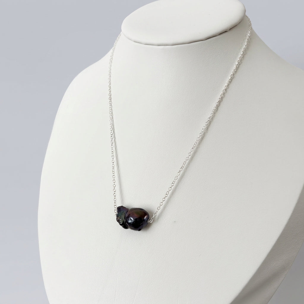 Dark blue Keshi pearl on a fine sterling silver chain, displayed on an angled white jewellery bust against a pale grey background.