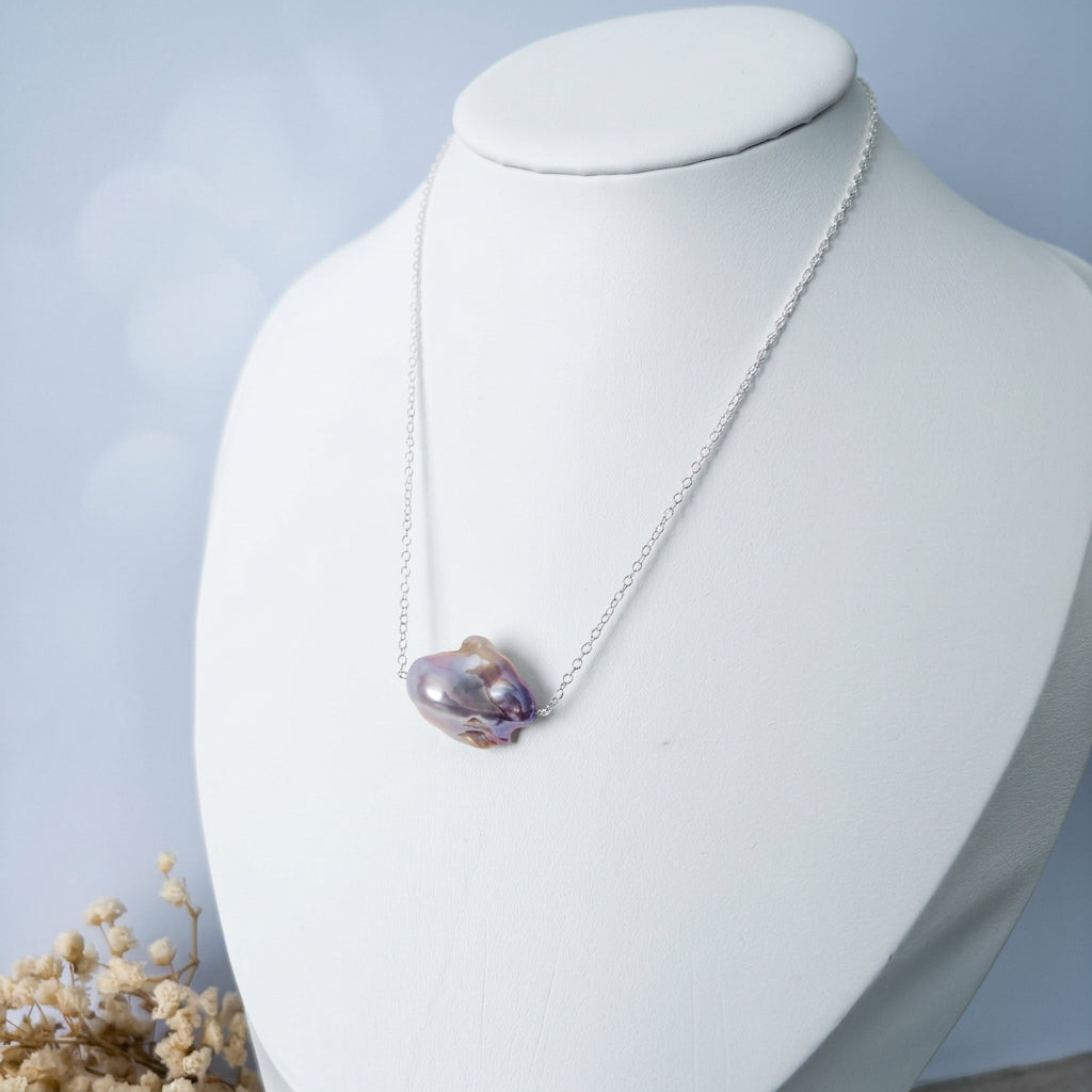 Pink Keshi pearl necklace displayed on a white jewellery bust, showing a single irregular pearl with mauve-pink lustre on a fine chain, with dried flowers beside the display.