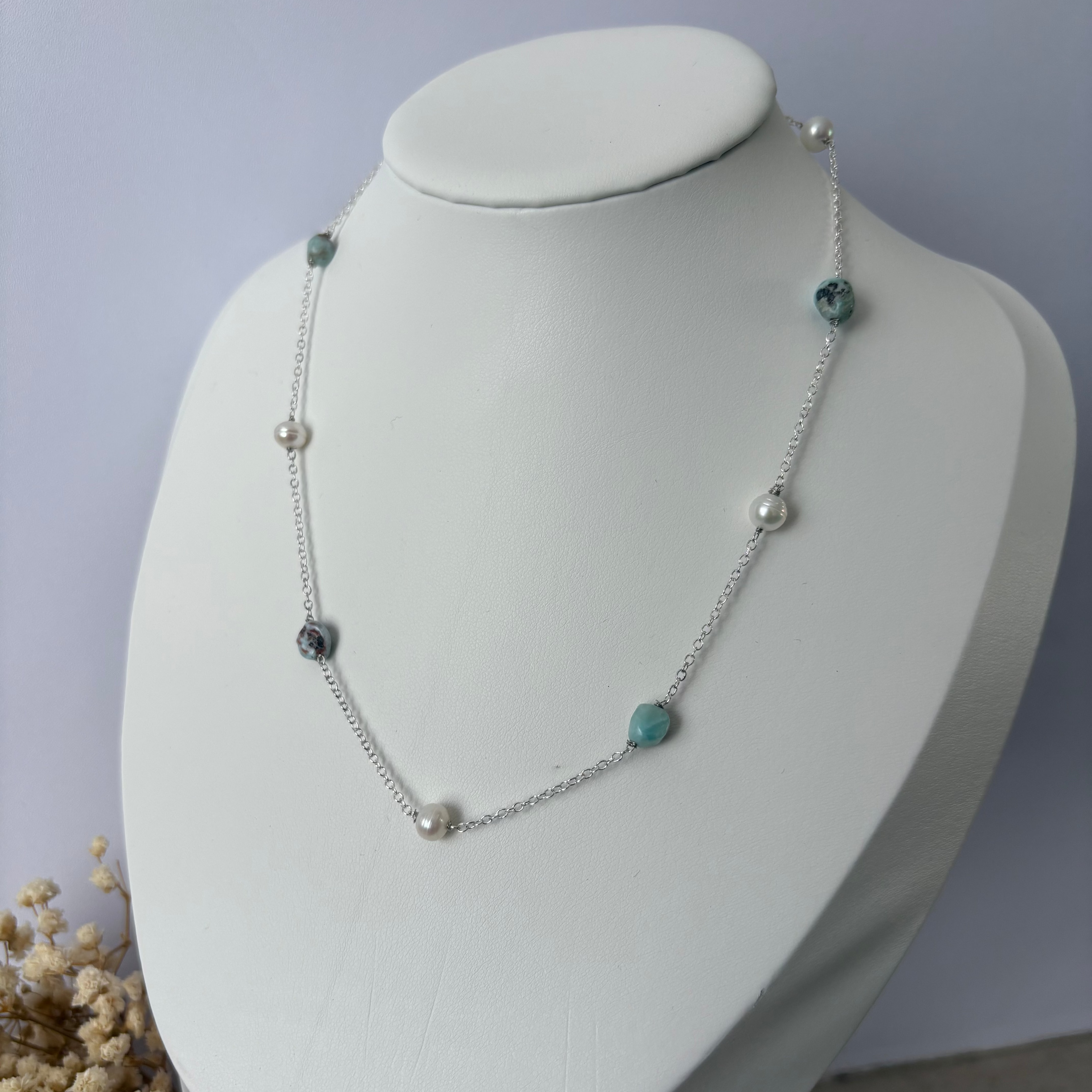 Pearl and larimar station necklace on a sterling silver chain, displayed on a white jewellery bust with dried flowers at its base against a pale grey background.⠋