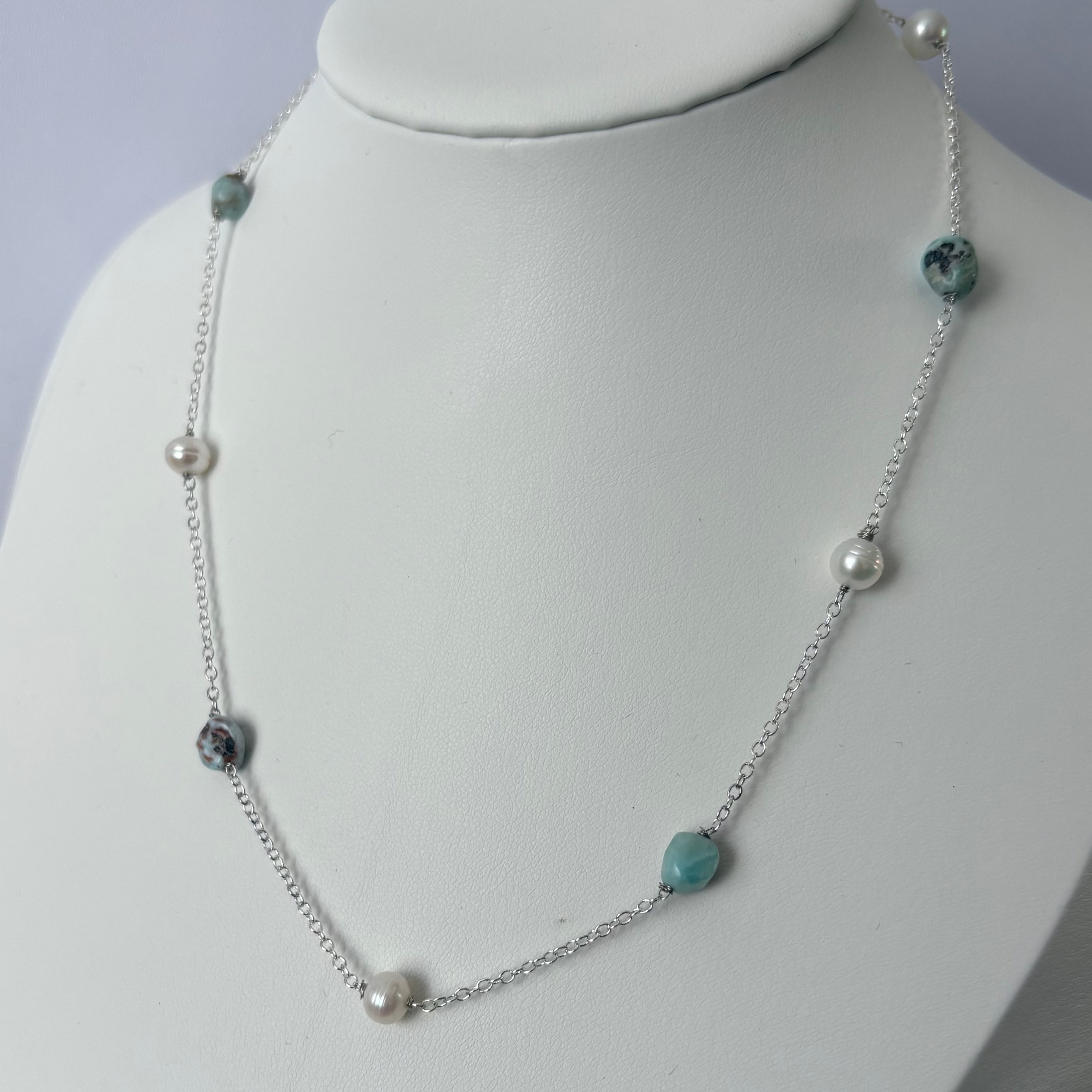 White baroque pearls and blue larimar stones with dark natural markings alternating along a sterling silver chain, displayed on an angled white jewellery bust.