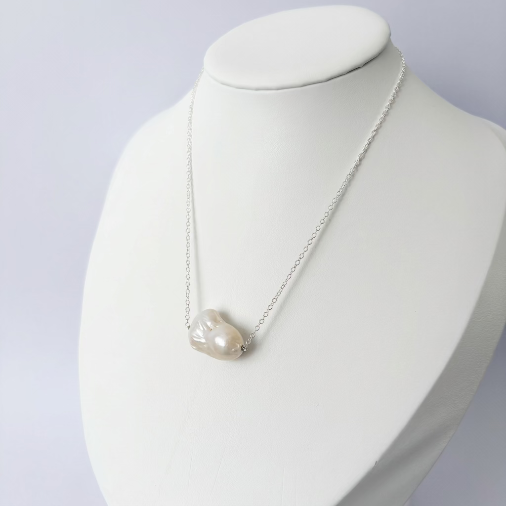 White Keshi pearl on a fine sterling silver chain, displayed on an angled white jewellery bust, showing the pearl’s organic shape and soft iridescent sheen.