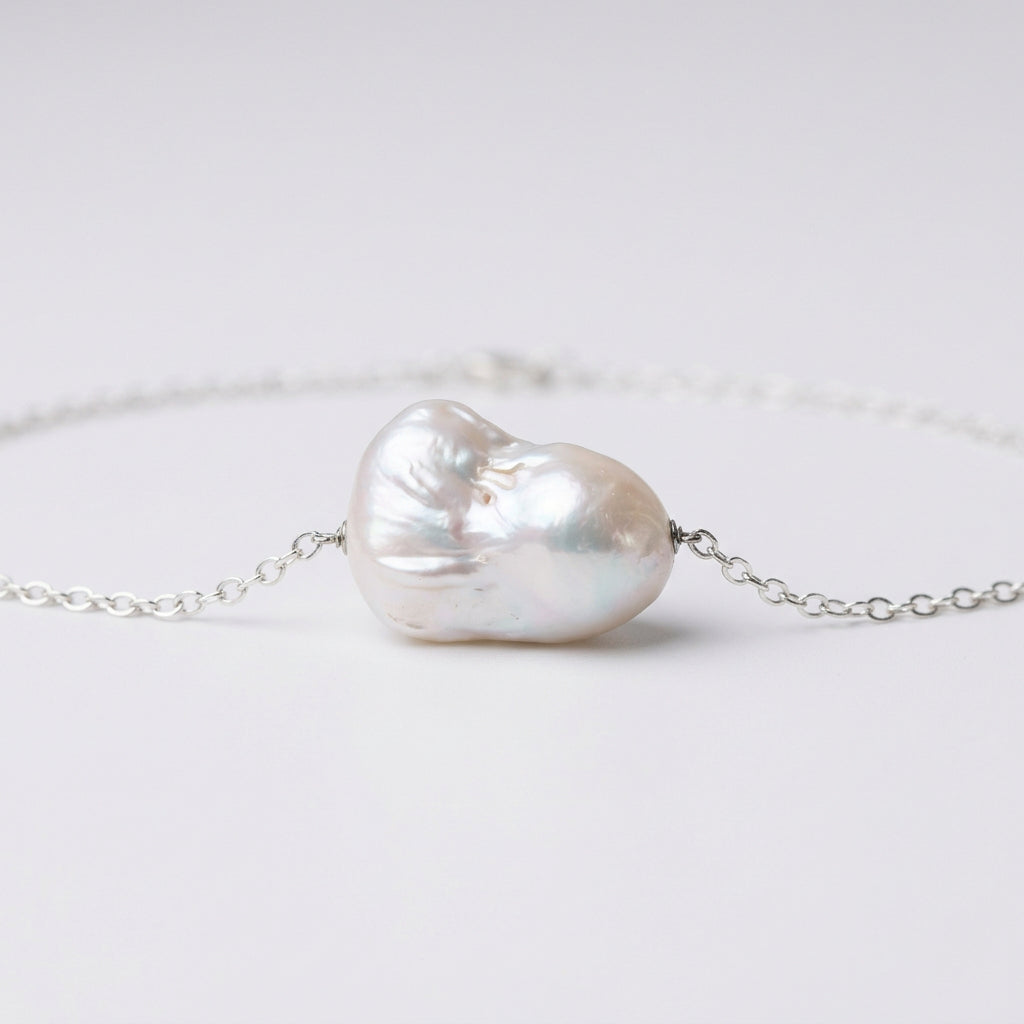 Close-up of a white Keshi pearl necklace resting on a white surface, showing the pearl’s irregular contours, soft iridescent lustre and sterling silver chain connections.