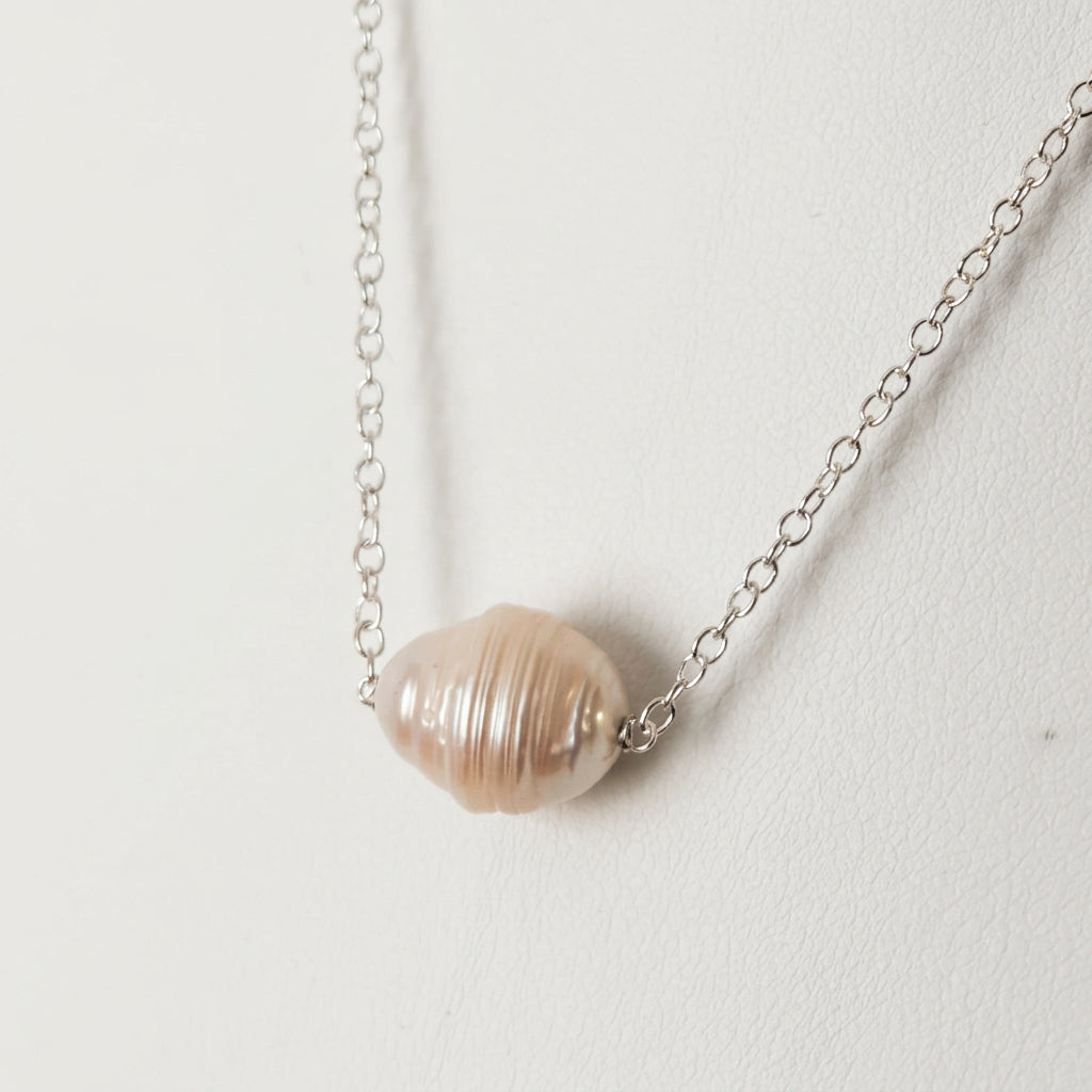 Close-up of a white baroque pearl with pronounced natural ringed ridges and warm ivory lustre, set directly on a fine sterling silver chain against a white jewellery bust.⠋