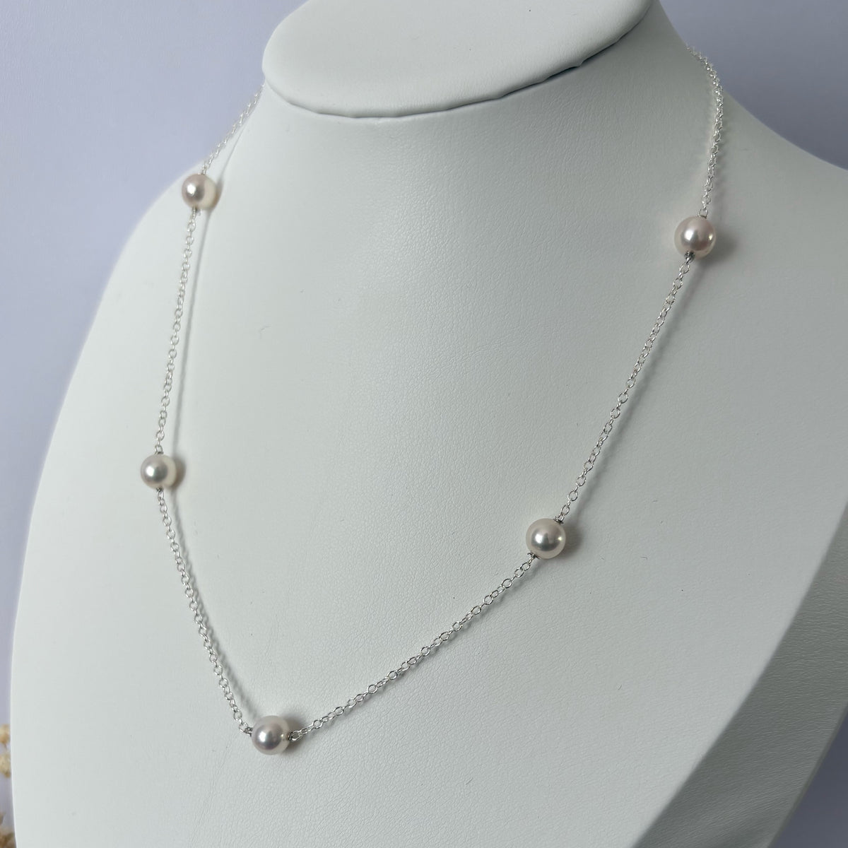 Close-up of an Akoya pearl station necklace on a white jewellery bust, showing five lustrous round white pearls spaced along a fine sterling silver chain.⠋