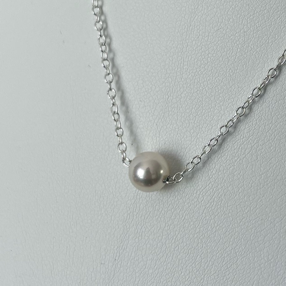 Angled close-up of a single white Akoya pearl necklace worn with a white top, showing the round, lustrous pearl set directly on a fine sterling silver chain.