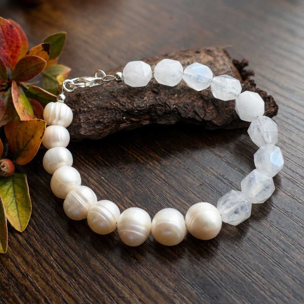 White baroque pearl and faceted clear quartz bracelet with a sterling silver lobster clasp, arranged on a wooden surface beside bark and autumn leaves.