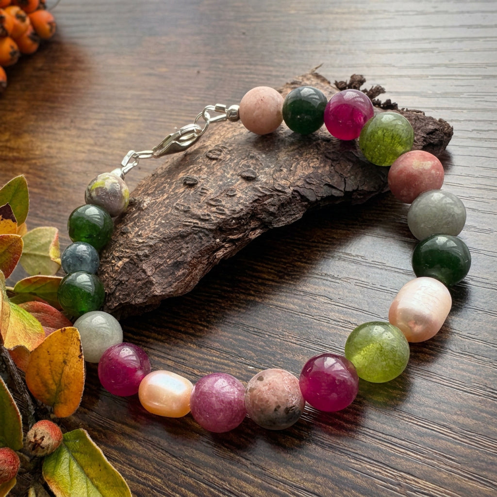Jasper, tourmaline and blush baroque pearl bracelet with a sterling silver lobster clasp, arranged on a wooden surface beside bark and autumn leaves.