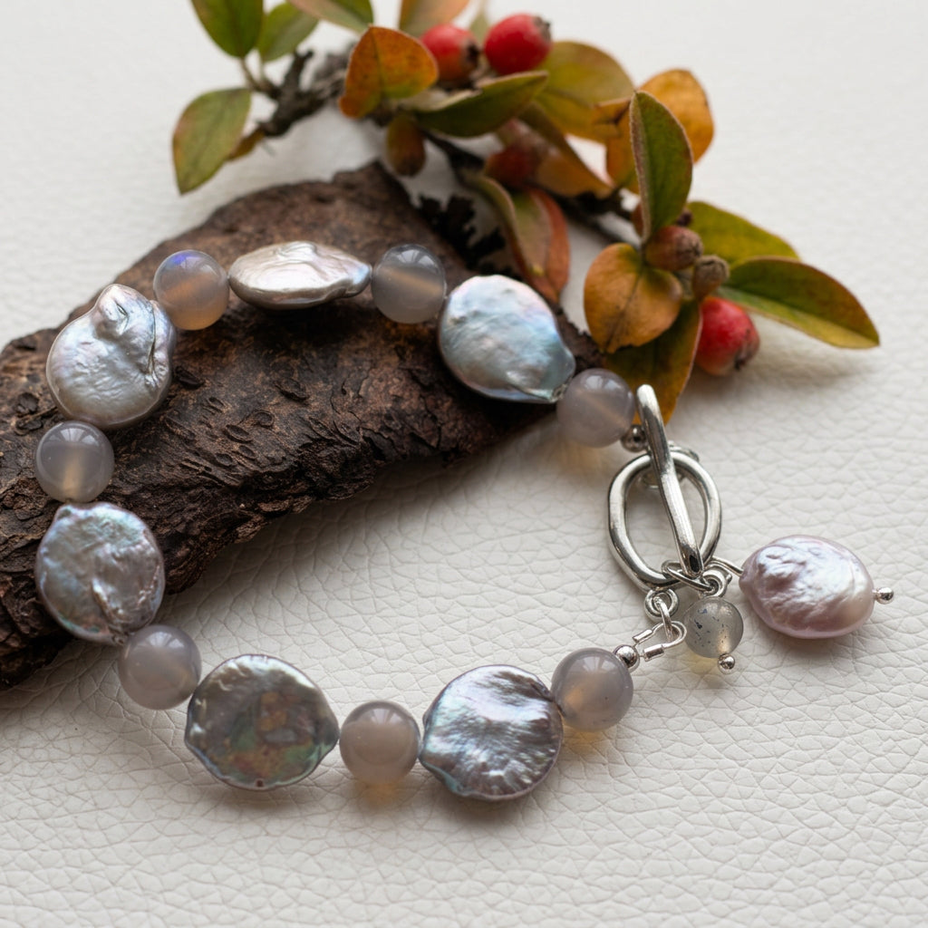 Labradorite and silver-toned coin pearl bracelet arranged beside bark, autumn leaves and red berries, with a fastened stainless steel toggle clasp and dangling pearl and labradorite charms.