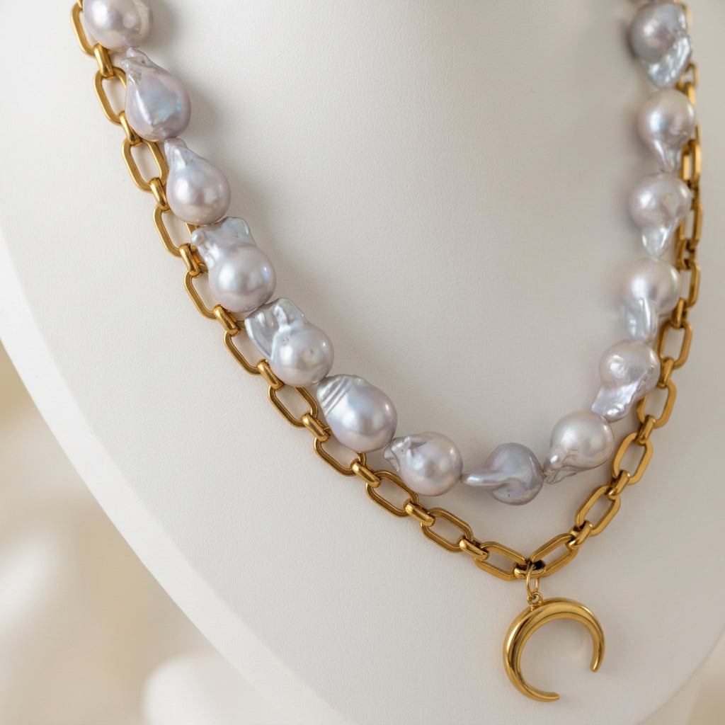 Double-layer necklace displayed on a white bust, featuring large silvery-white keshi pearls above a gold-plated paperclip chain with a downward-pointing crescent moon pendant.