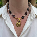 Deep burgundy garnet stones alternating with white rice pearls, with a fastened gold-plated front toggle clasp, two garnet drops and a sun-and-crescent-moon pendant, worn with an open-neck white shirt.