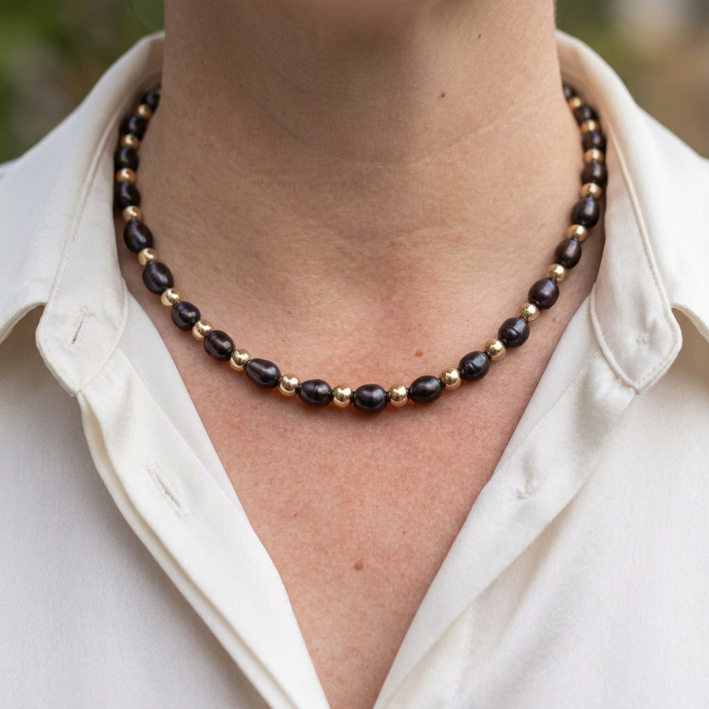 Deep purple rice pearls alternating with round gold-coloured hematite beads, worn at the collarbone with an open-neck white shirt.
