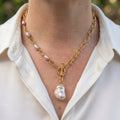 Gold-plated oval-link necklace with four mauve rice pearls along one side, a fastened front toggle and a large cream keshi pearl pendant, worn with an open-neck white shirt.