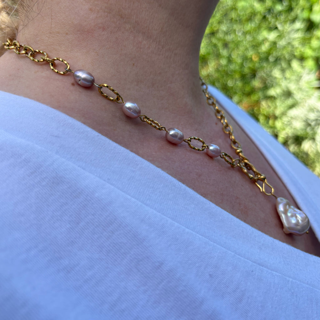 Angled view of a keshi pearl pendant necklace worn outdoors with a white top, showing four freshwater rice pearls spaced along one side of the gold-coated oval-link chain.