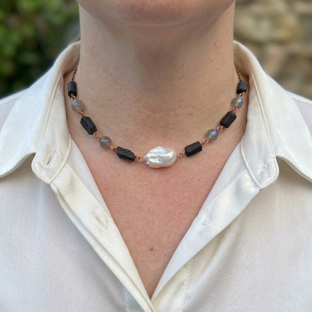 White keshi pearl, raw black tourmaline and labradorite necklace worn with an open-neck white shirt, featuring an irregular white pearl centrepiece, grey beads with blue flashes and handmade copper wire links.