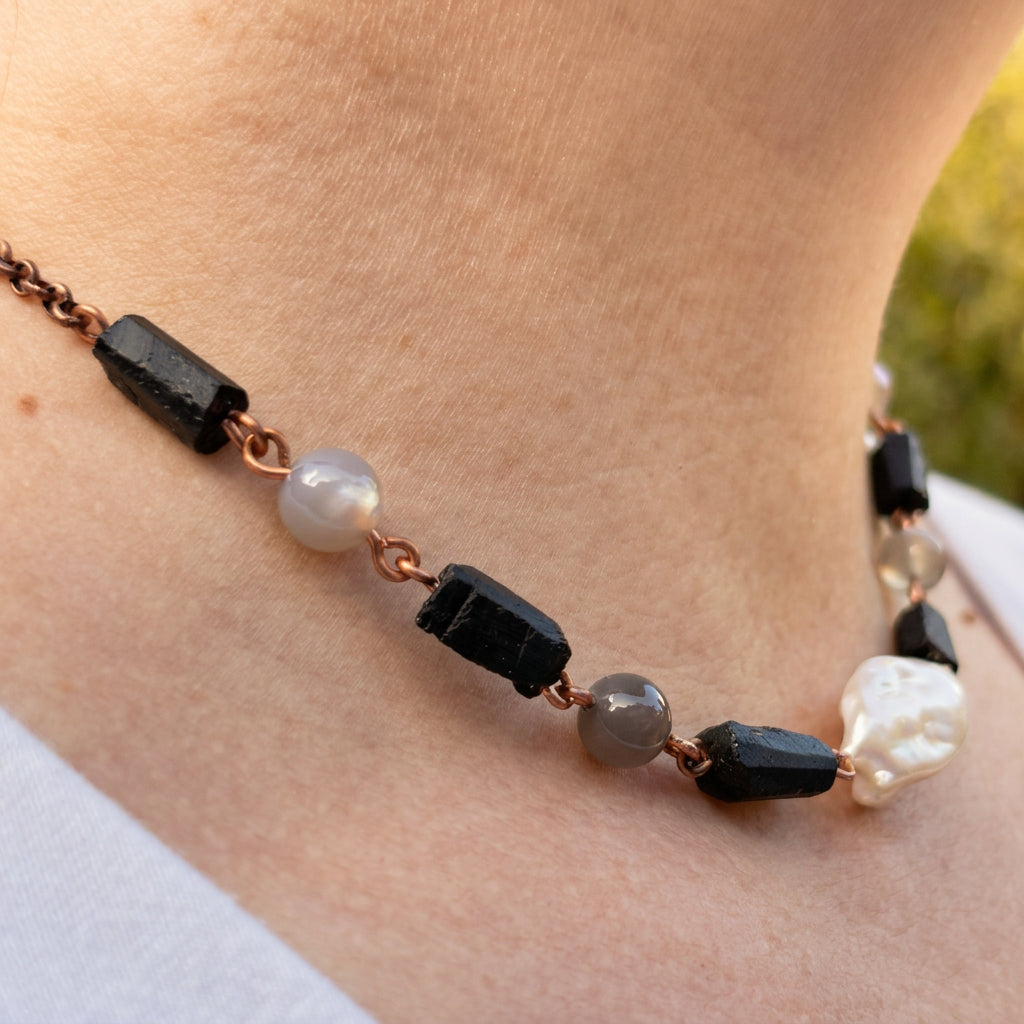 Side view of a copper wire necklace worn at the collarbone, showing raw black tourmaline crystals, round grey labradorite beads and a large white Keshi pearl.