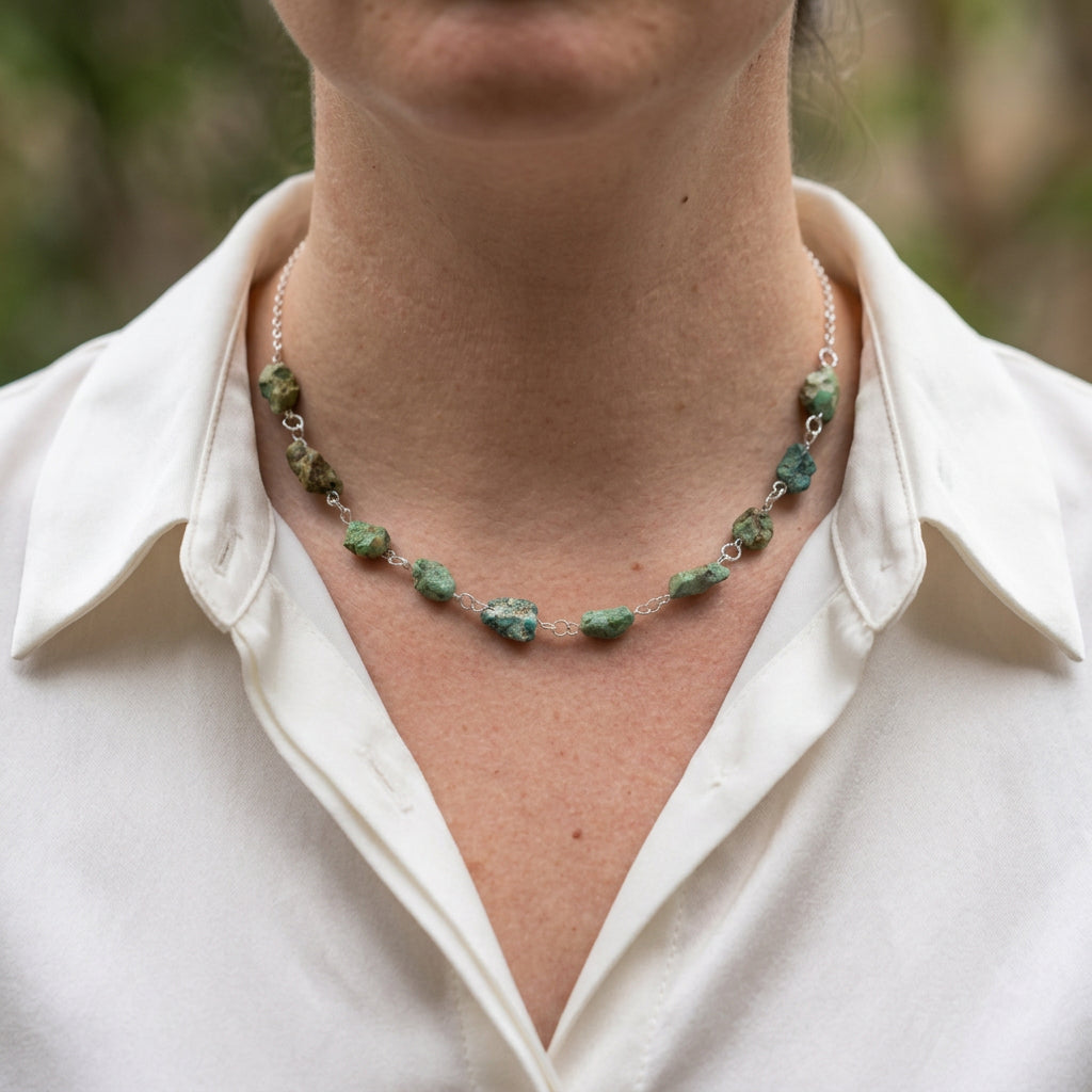 Raw Hubei turquoise necklace worn with an open-neck white shirt, showing ten irregular green-blue stones with earthy brown matrix, joined by handmade sterling silver wire links and a fine silver chain.