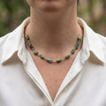 Raw Hubei turquoise necklace worn with an open-neck white shirt, showing ten irregular green-blue stones with earthy brown matrix, joined by handmade sterling silver wire links and a fine silver chain.
