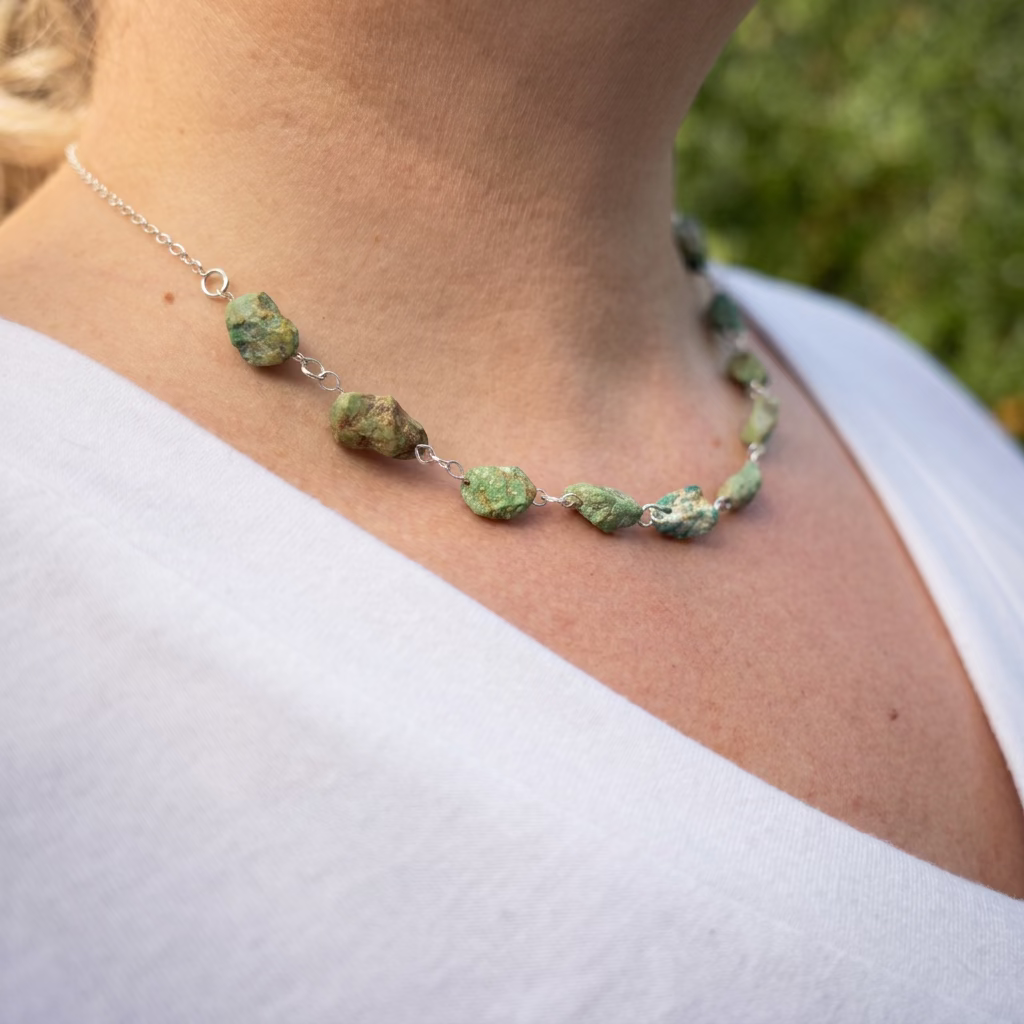Side view of a raw Hubei turquoise necklace worn with a white V-neck top, showing rough green-blue stones with brown matrix, handmade sterling silver wire links and a fine silver chain along the neckline.