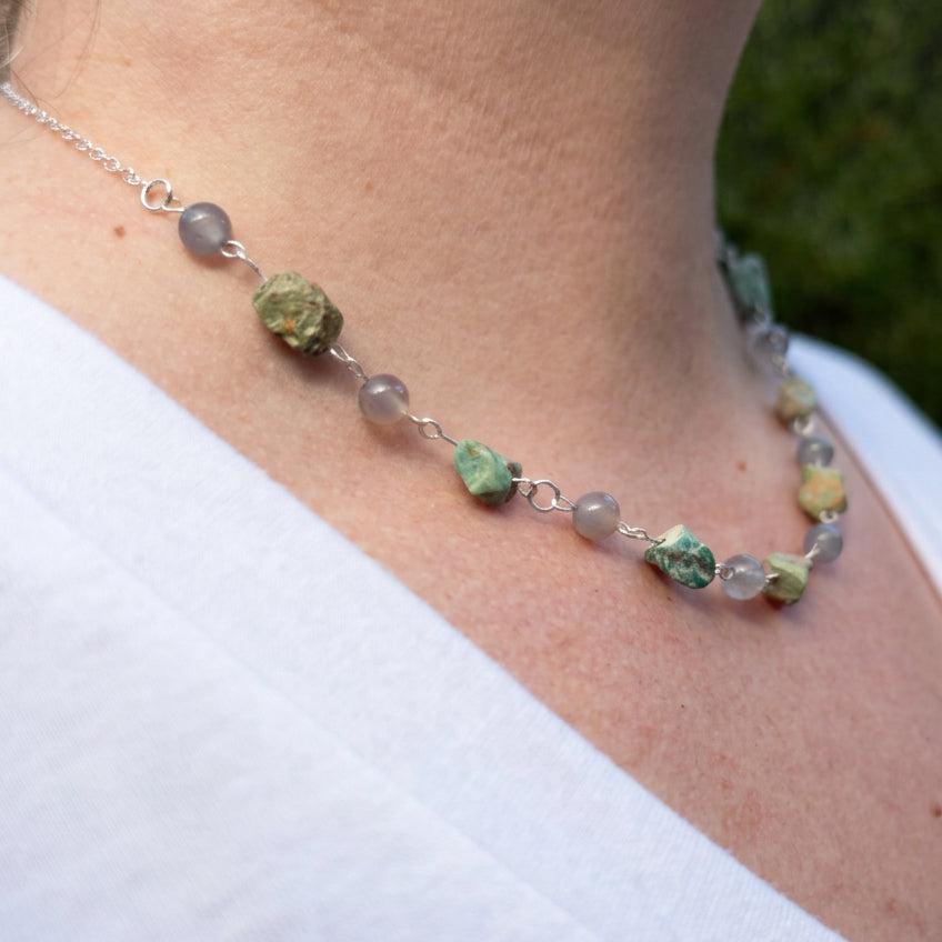 Side view of a sterling silver necklace worn at the collarbone, with raw green-blue Hubei turquoise stones alternating with round grey labradorite beads.