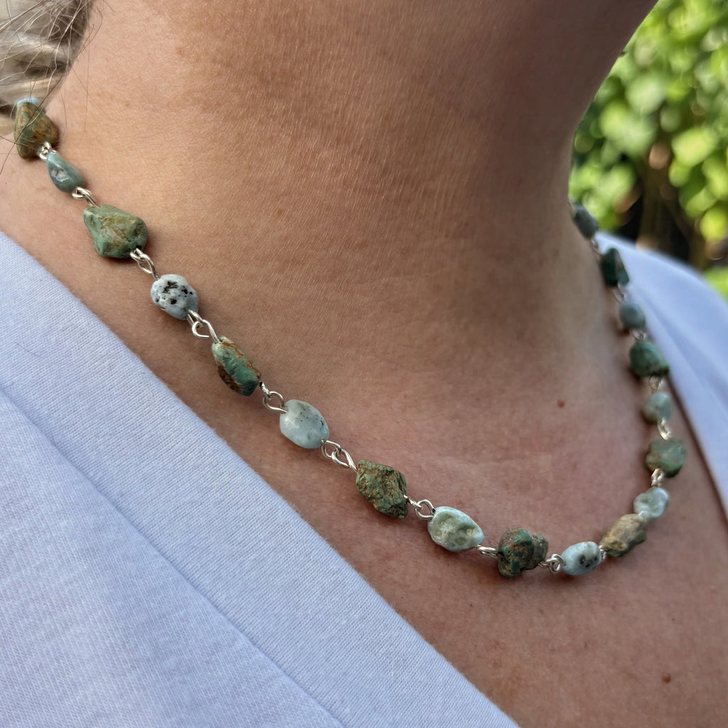 Side view of a sterling silver necklace worn below the collarbone, with raw green Hubei turquoise stones alternating with pale blue larimar beads with dark markings.⠋