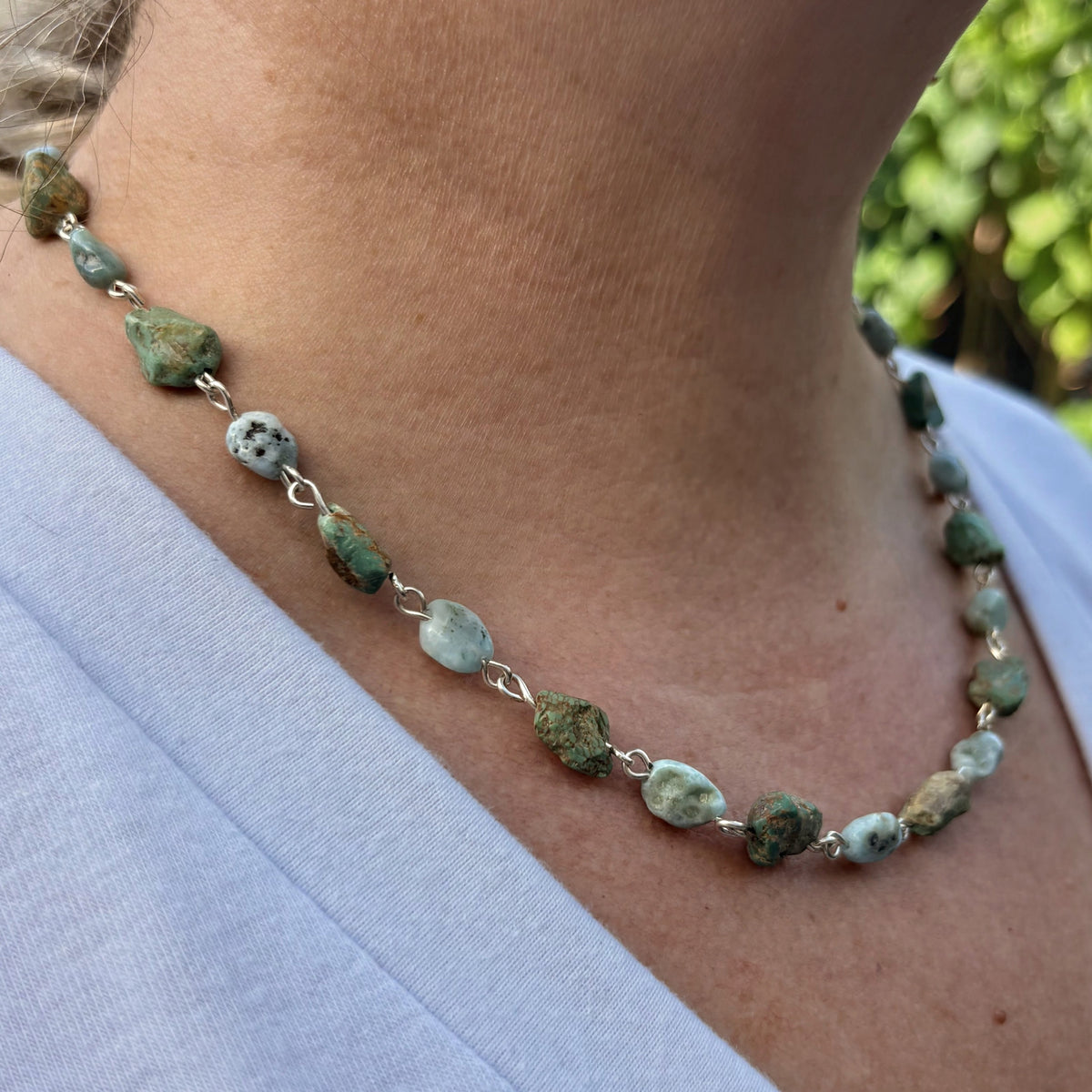 Side view of a sterling silver necklace worn below the collarbone, with raw green Hubei turquoise stones alternating with pale blue larimar beads with dark markings.⠋