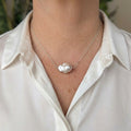 Large blush-pink keshi pearl on a delicate chain, worn with an open-neck white shirt, showing the pearl’s irregular petal-like shape and silvery iridescent lustre.