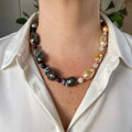 Statement necklace with dark blue-grey keshi pearls along one side and golden-cream keshi pearls along the other, separated by small purple, navy and pale pink gemstone beads, worn with an open-neck white shirt.