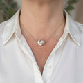 Pink keshi pearl necklace on a delicate gold-filled chain, worn with an open-neck white shirt, showing an irregular petal-shaped pearl with blush tones and bright silvery lustre.