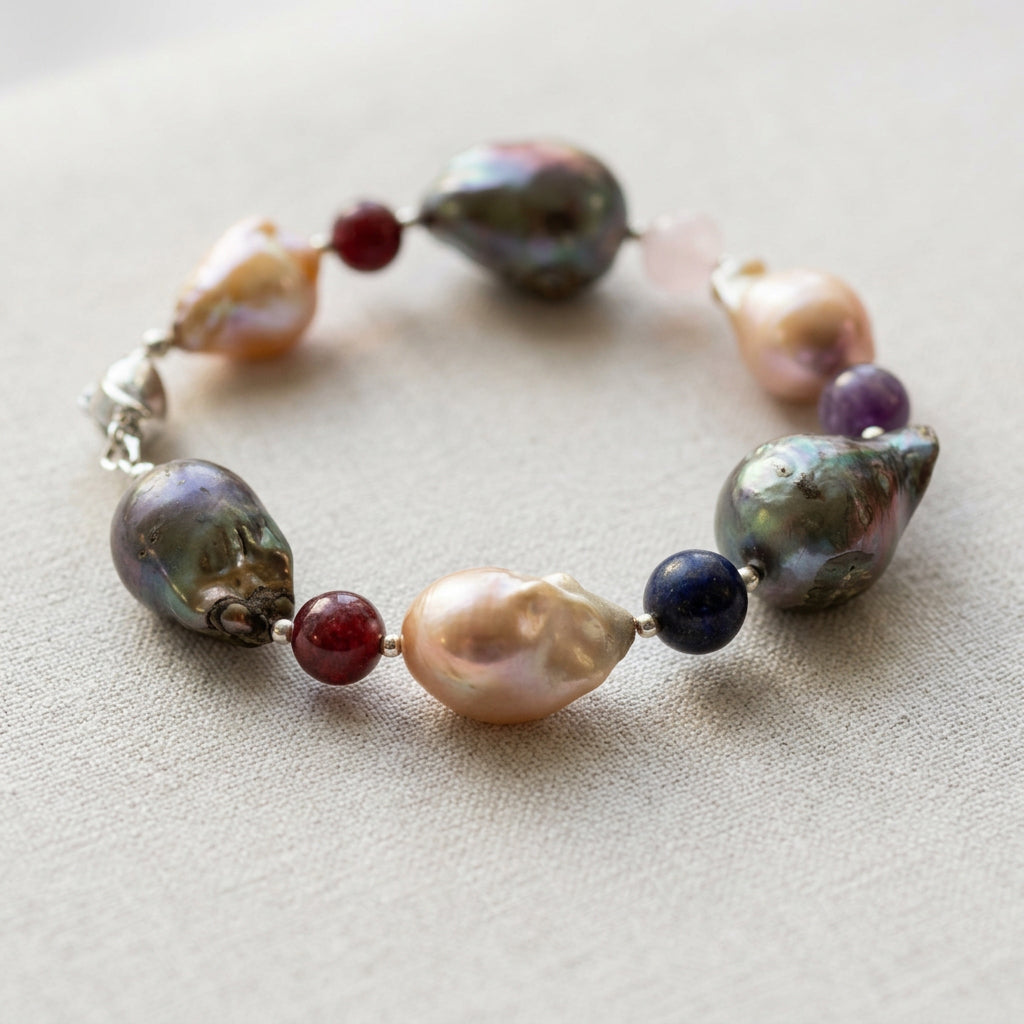 Keshi pearl bracelet arranged in an oval on pale linen, showing alternating dark iridescent and blush-cream pearls with red garnet, deep blue lapis lazuli, purple amethyst, pale pink quartz and sterling silver accents.