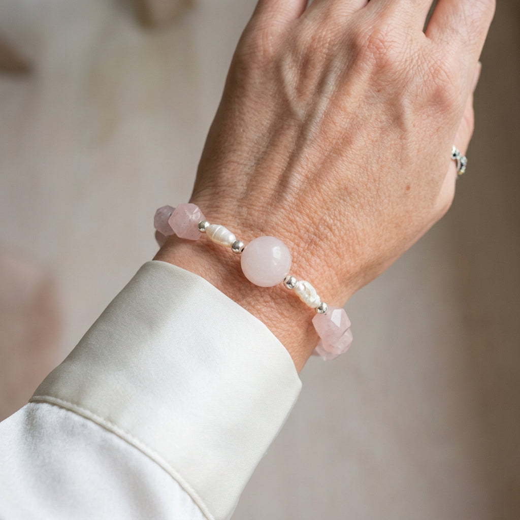 Pale pink quartz bracelet with a large round centre bead, faceted pink beads, white freshwater pearls and silver-coloured hematite spacers, worn beside a white silk shirt cuff.
