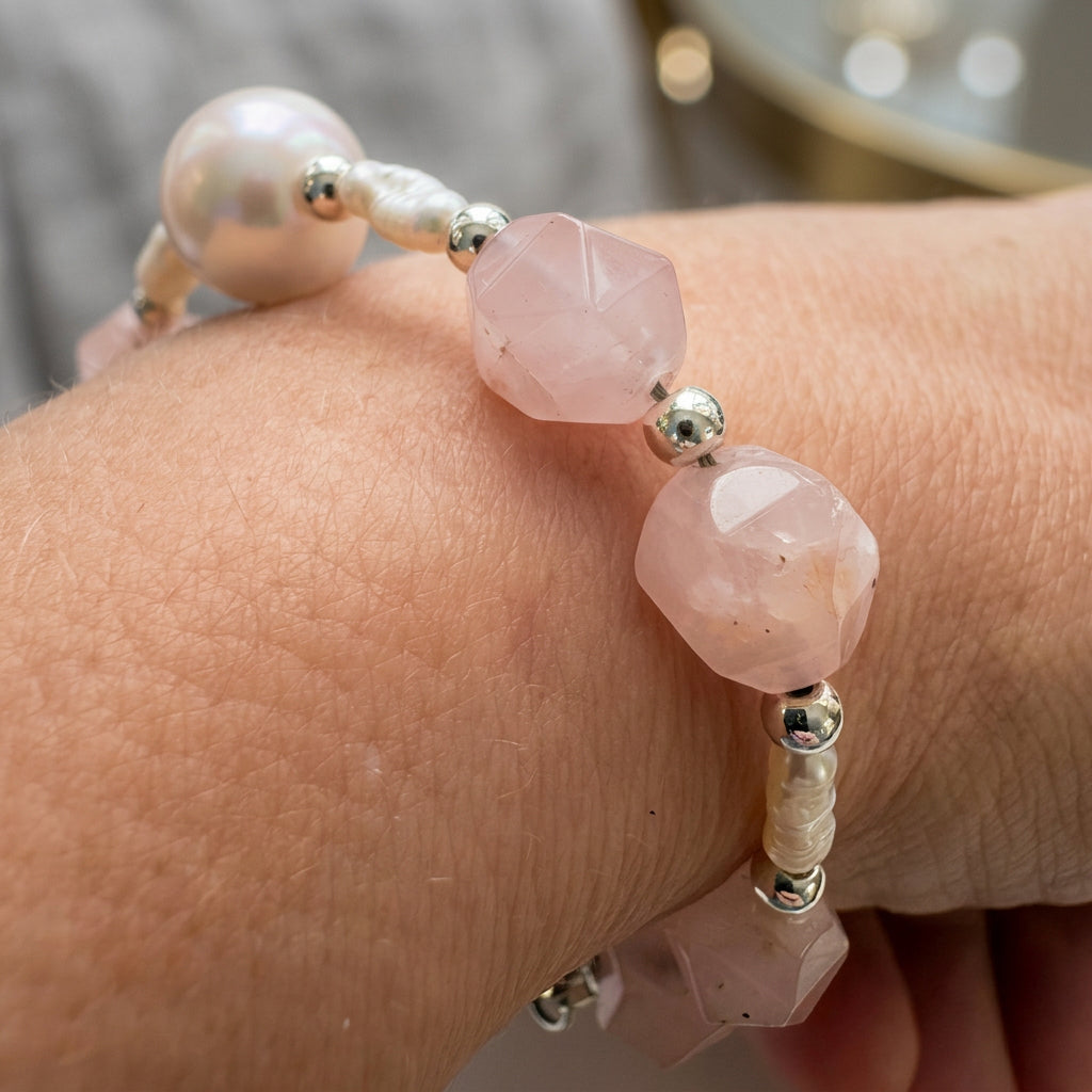 Close-up of a pink quartz and pearl bracelet worn on a wrist, showing natural inclusions in the faceted pale pink beads, ribbed white rice-shaped pearls and polished silver-coloured hematite spacers.