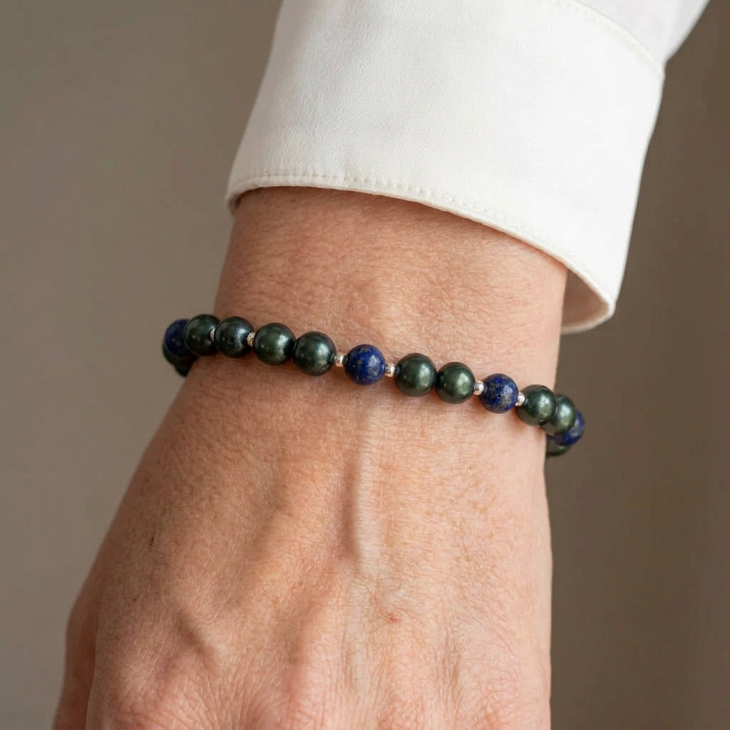 Deep green peacock pearls and blue lapis lazuli beads with small sterling silver spacers, worn as a bracelet beside a white silk shirt cuff.