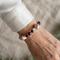 Blush-cream keshi pearl bracelet with black onyx, burgundy garnet and pale quartz beads, worn on the wrist beside a white silk shirt cuff.