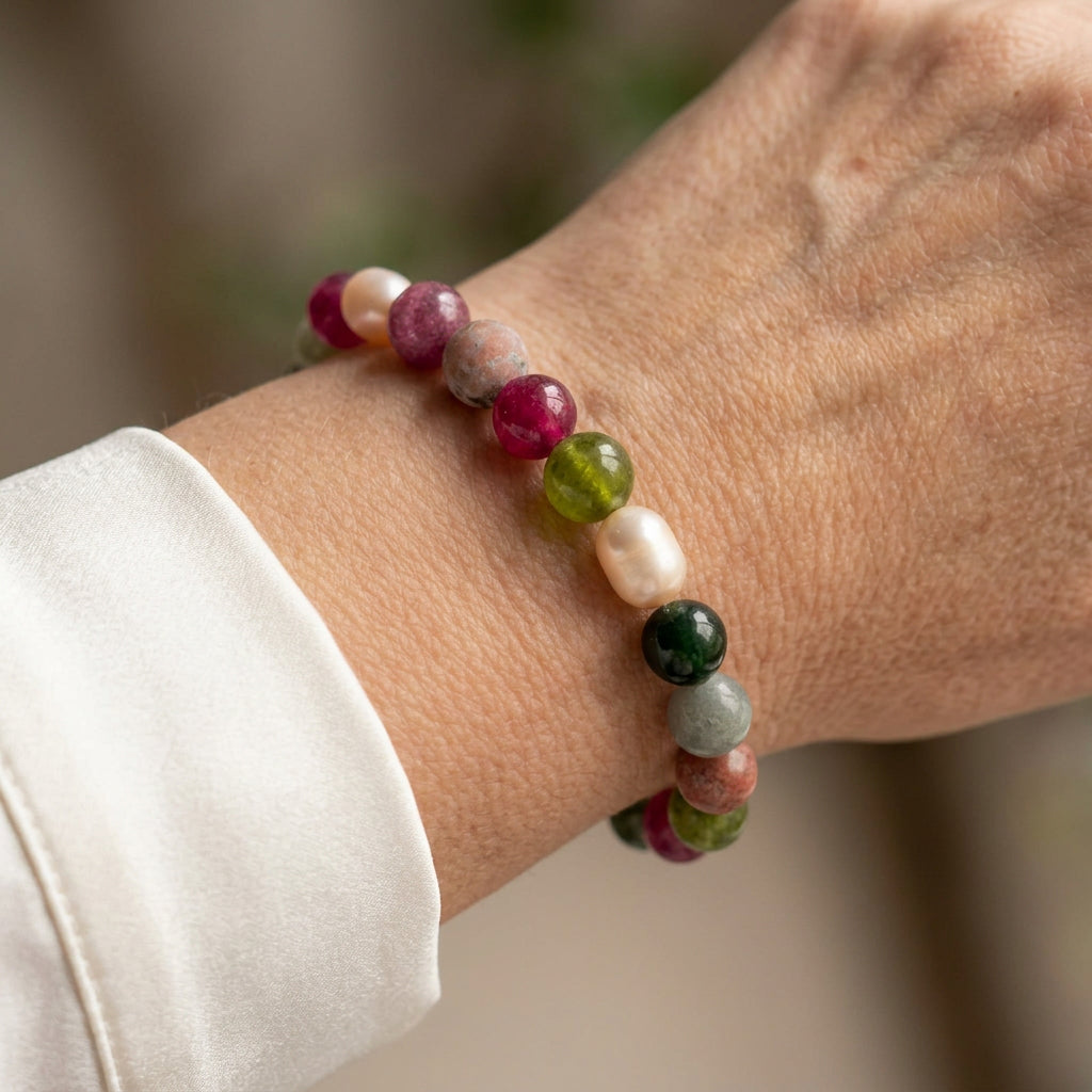 Multicoloured jasper and tourmaline bracelet with pink, green and grey beads and creamy white baroque pearls, worn on the wrist beside a white silk shirt cuff.