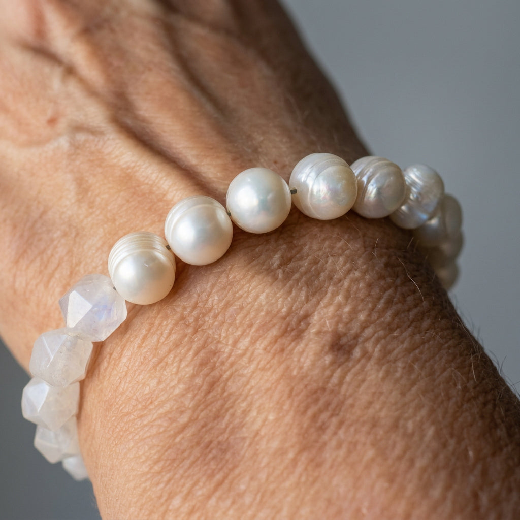 Close-up of a creamy white baroque pearl and clear quartz bracelet worn on a wrist in natural light, highlighting the pearls’ lustre and the quartz beads’ angular facets.