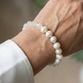 Creamy white baroque pearl bracelet with a section of irregular translucent clear quartz beads, worn on the wrist beside a white silk shirt cuff.