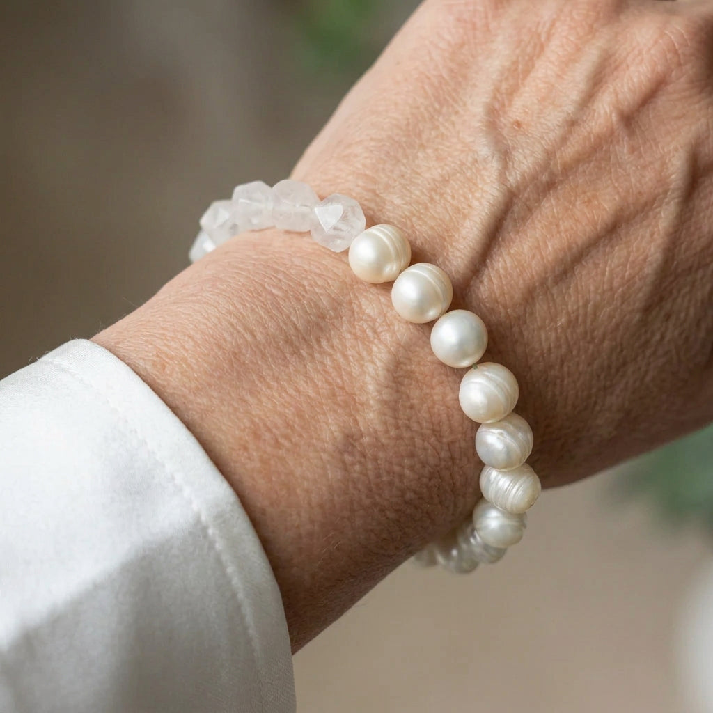 Creamy white baroque pearl bracelet with a section of irregular translucent clear quartz beads, worn on the wrist beside a white silk shirt cuff.