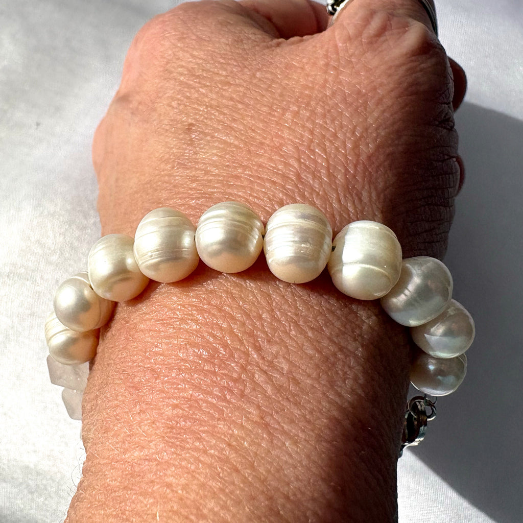 White baroque pearl and clear quartz bracelet worn on a wrist in bright sunlight, highlighting the pearls’ creamy lustre, irregular shapes and pronounced natural ridges.