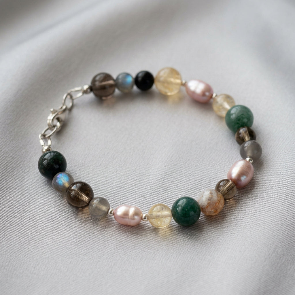 Pink baroque pearl and gemstone bracelet arranged in an oval on grey fabric, with pale yellow citrine, smoky brown quartz, green beads, blue-flashing labradorite and a sterling silver lobster clasp.
