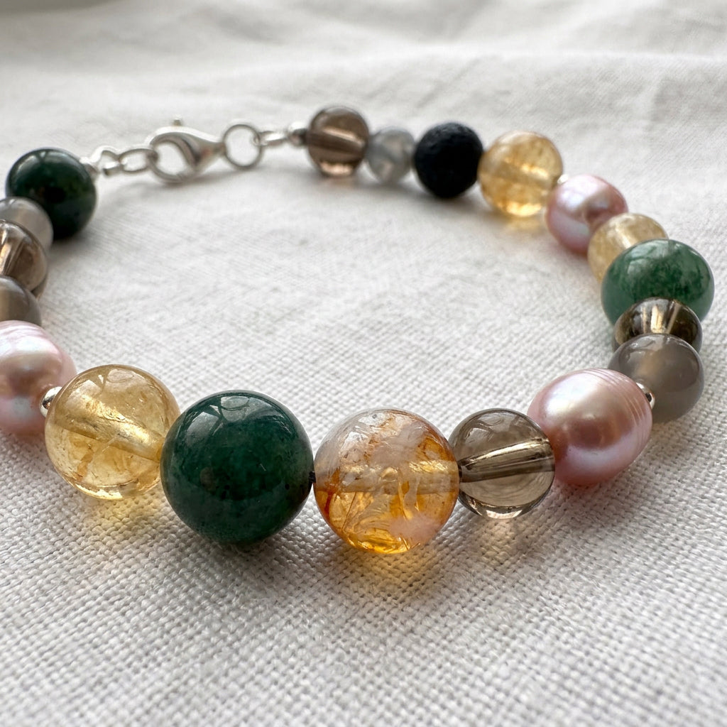 Pink baroque pearl and gemstone bracelet arranged in a circle on pale linen, showing honey-yellow citrine, mottled green, smoky brown and pale grey beads with a sterling silver lobster clasp.
