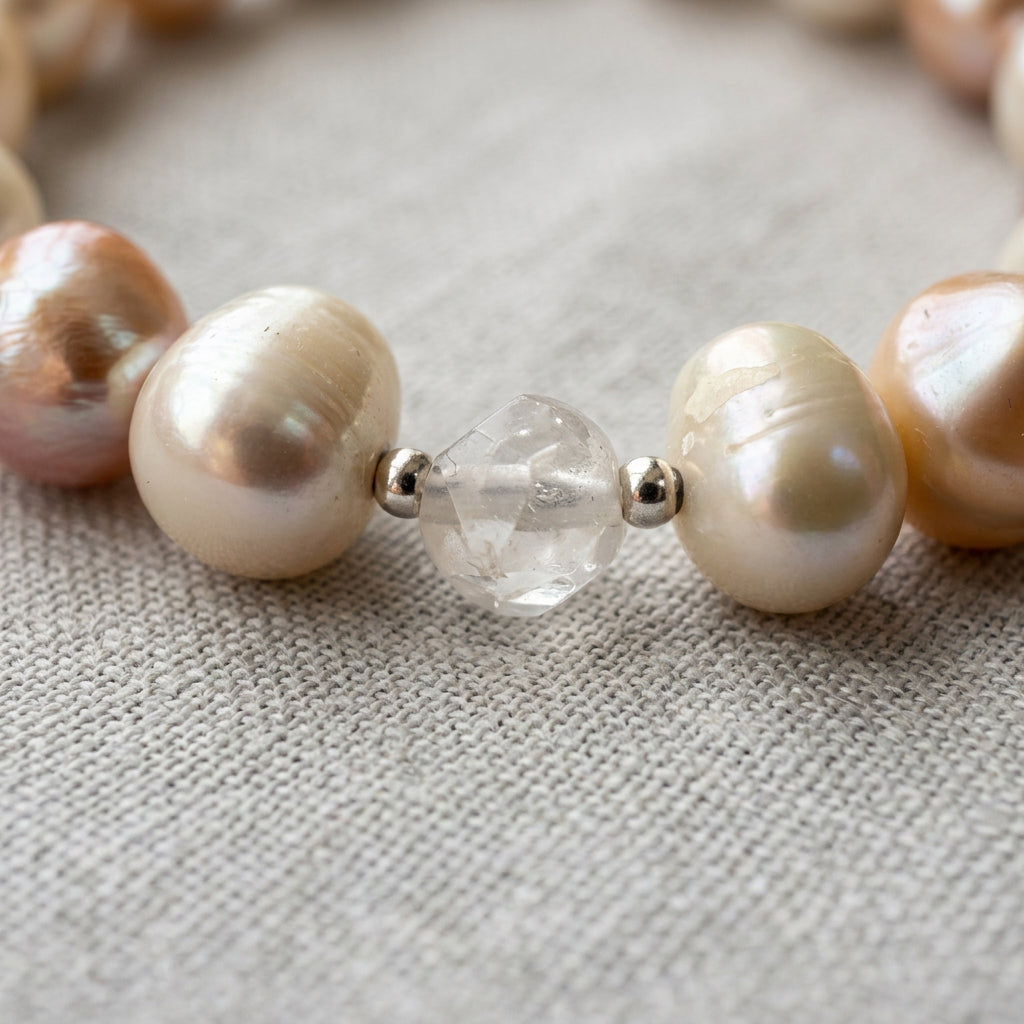 Close-up of a faceted clear quartz bead between sterling silver spacers and two creamy white baroque pearls, showing their natural ridges and lustre on grey linen.