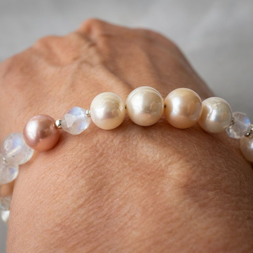 Close-up of a bracelet worn on a wrist, showing creamy white and blush pink baroque pearls beside faceted clear quartz beads and small sterling silver spacers.