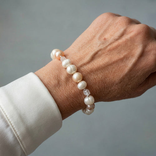 Creamy white baroque pearl bracelet with faceted clear quartz accents and small silver-coloured spacers, worn on the wrist beside a white silk shirt cuff.